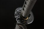 Demon-killing sword tsuba, black metal sword guard with intricate embossed figure. Complements black wrapped handle, provides protection and decoration.