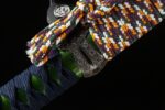 Shogun Tachi scabbard detail, focusing on the kurikata and the colorful sageo knot tied above it, with purple, white, gold, and green threads intertwined, showcasing the scabbard accessory's material and tying method.