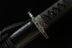 Buddha and Demon Sword handle-scabbard junction. Black tsuka-maki, metallic fuchi with texture and engraving, and koiguchi detail show refined craftsmanship.