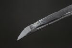 Close-up of the tip of a dark plum katana sword with a Damascus pattern